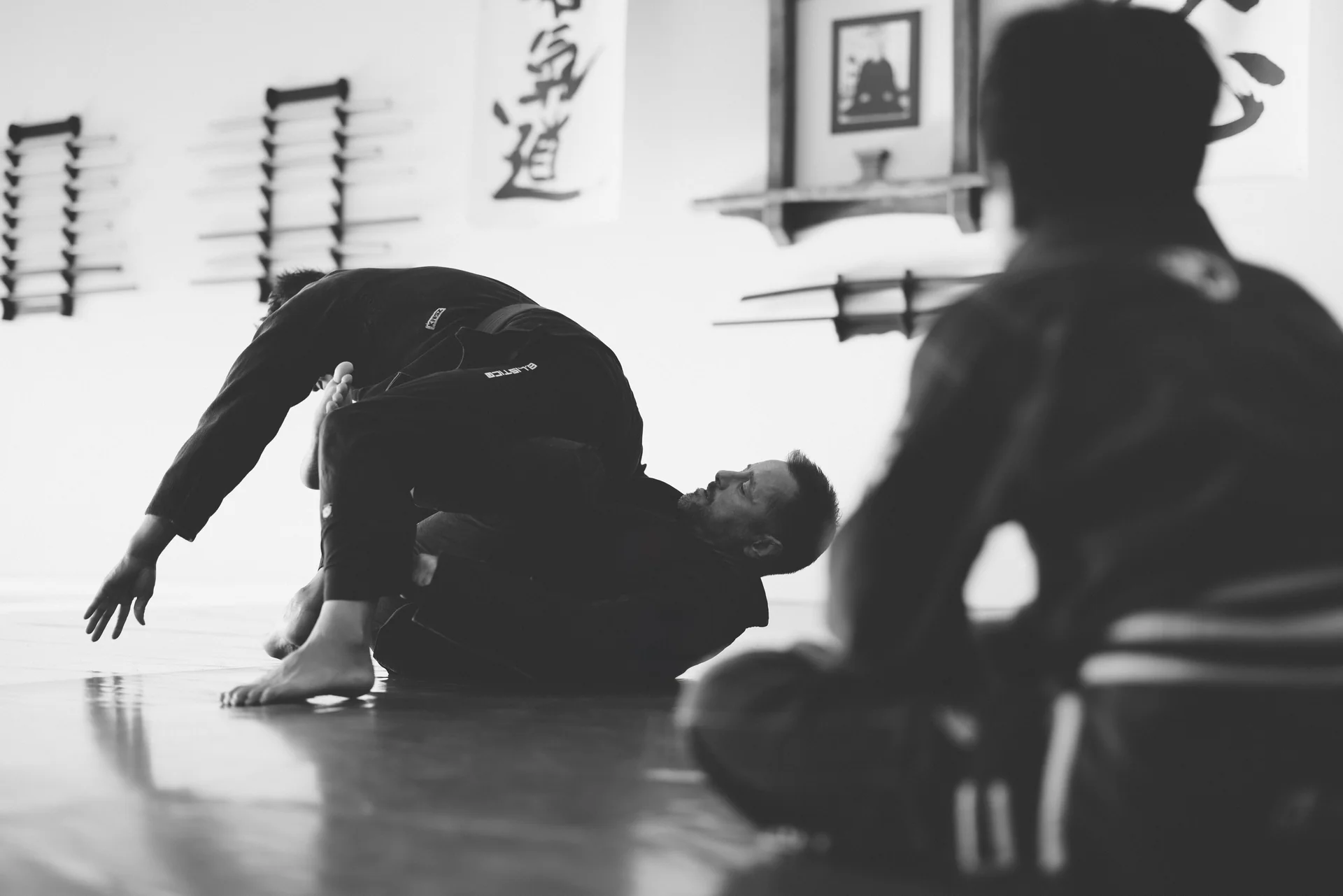 Jiu jitsu demonstration on the mats, watched by a student.