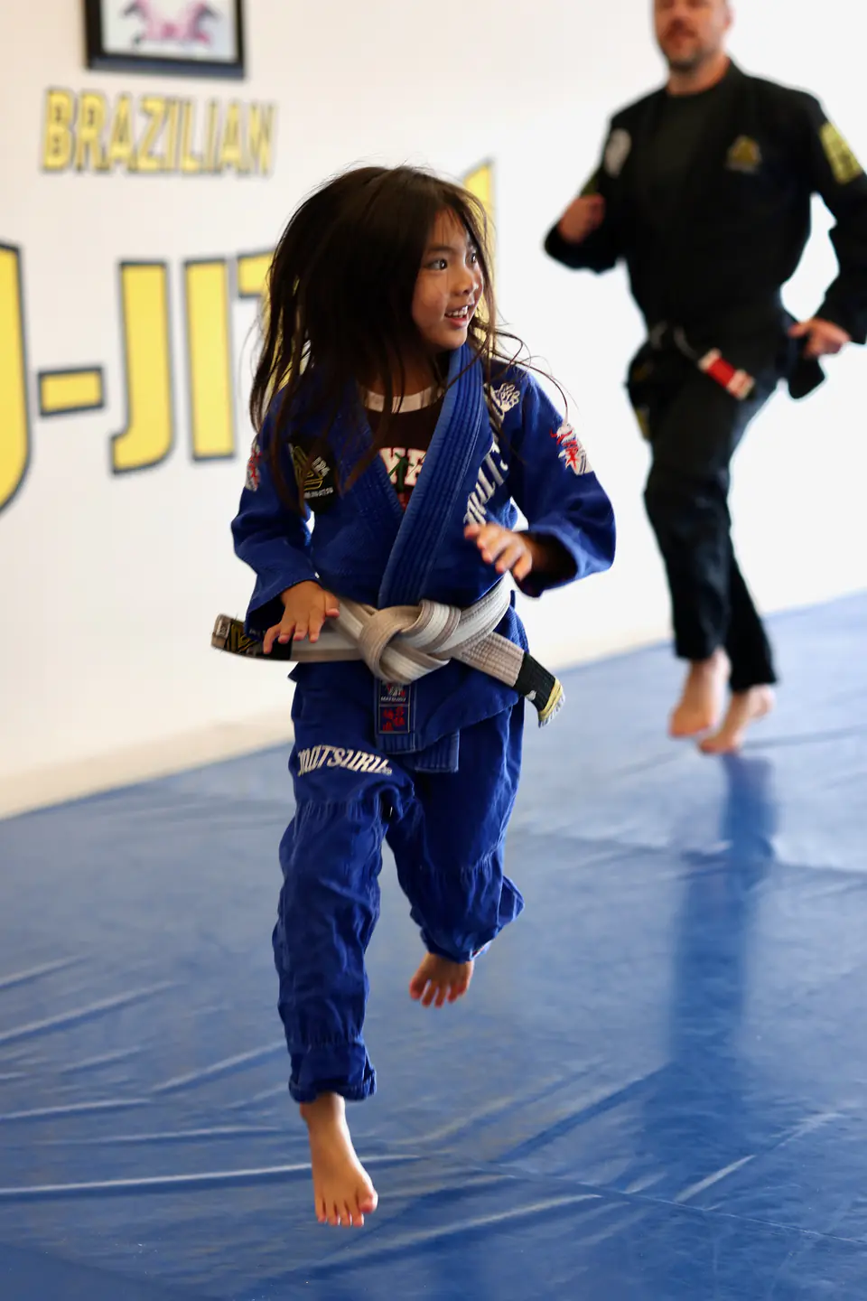 A young Munchkins student runs across the blue mats during a movement game